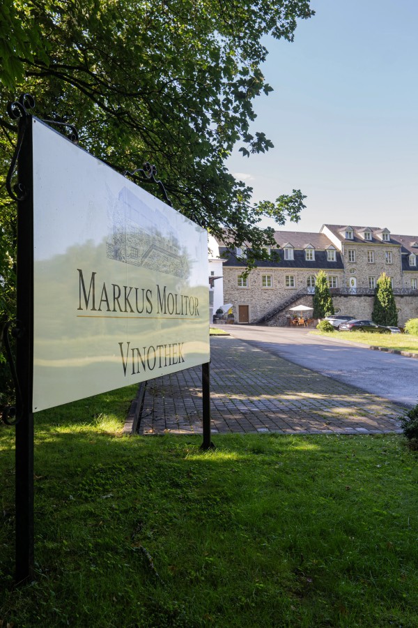 Schild mit der Aufschrift Markus Molitor Vinothek vor einem großen historischen Gebäude bei Sonnenschein