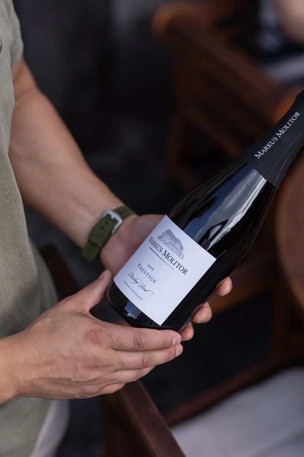Mann haelt eine Flasche Markus Molitor Prestige Riesling Brut Wein in beiden Haenden
