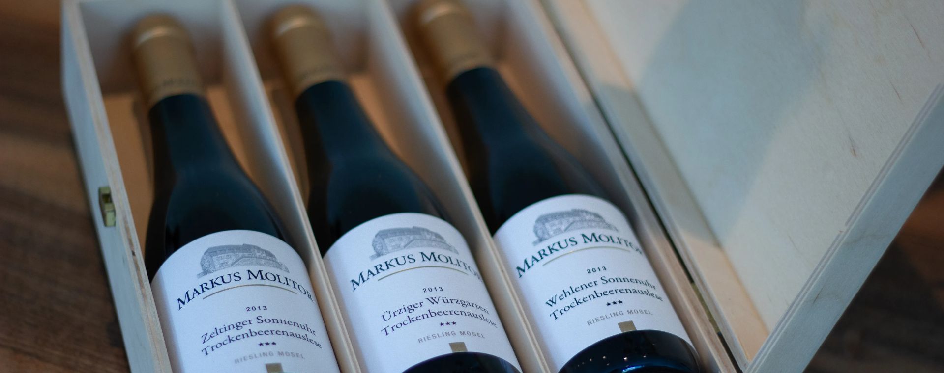 Drei Flaschen Markus Molitor Riesling Weine in einer offenen Holzbox auf Holztisch stehend